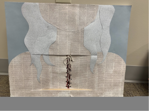 Image description: an example of a radical revision: a collage showing the lower half of a person’s head and their shoulders. The background is made of blue-gray paper with variegated lighter and darker shades. The person’s hair is made from silver paper, and the face, neck, and shoulders are made from paper with printed text. In the middle of the person’s chest is a vertical cut with holes at the edges. String is used to lace up and tie together the vertical cut.