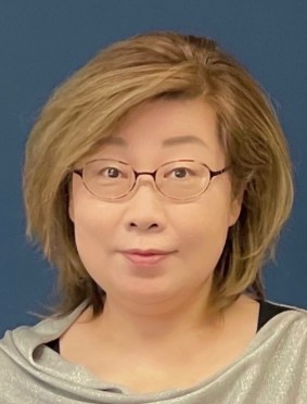 Julia Chen smiles at the camera and poses in front of a blue background