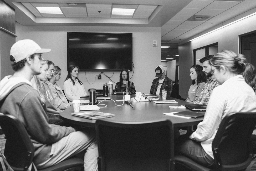Eleven James Madison University students are sitting around a conference table in meditation with their eyes closed during their tutor education course.