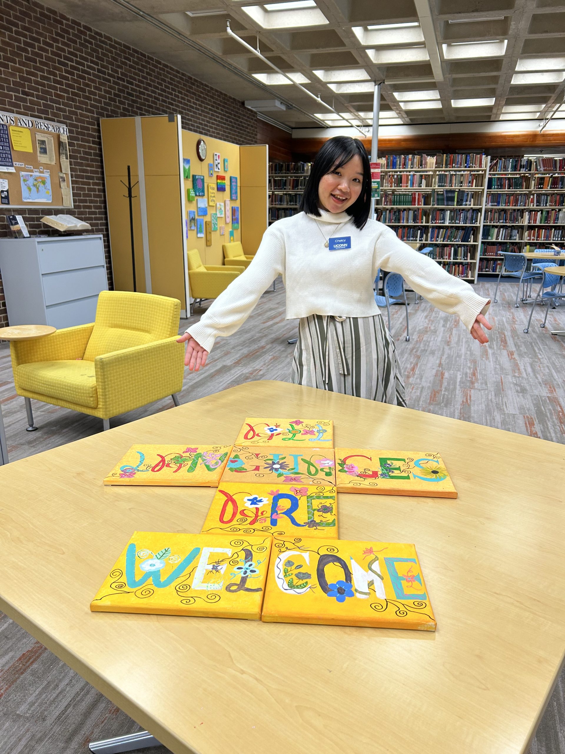 Photo of the artist, Chelcy, along with a painted sign that reads, "all languages are welcome."